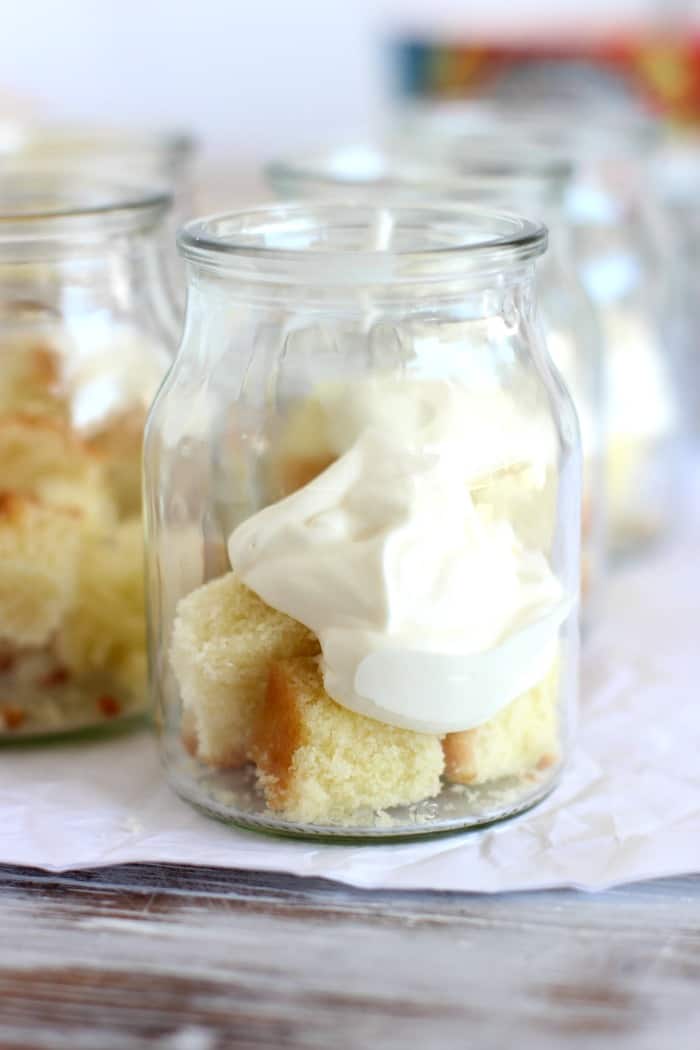 Close up glass jar with cake and whipped cream, white surface