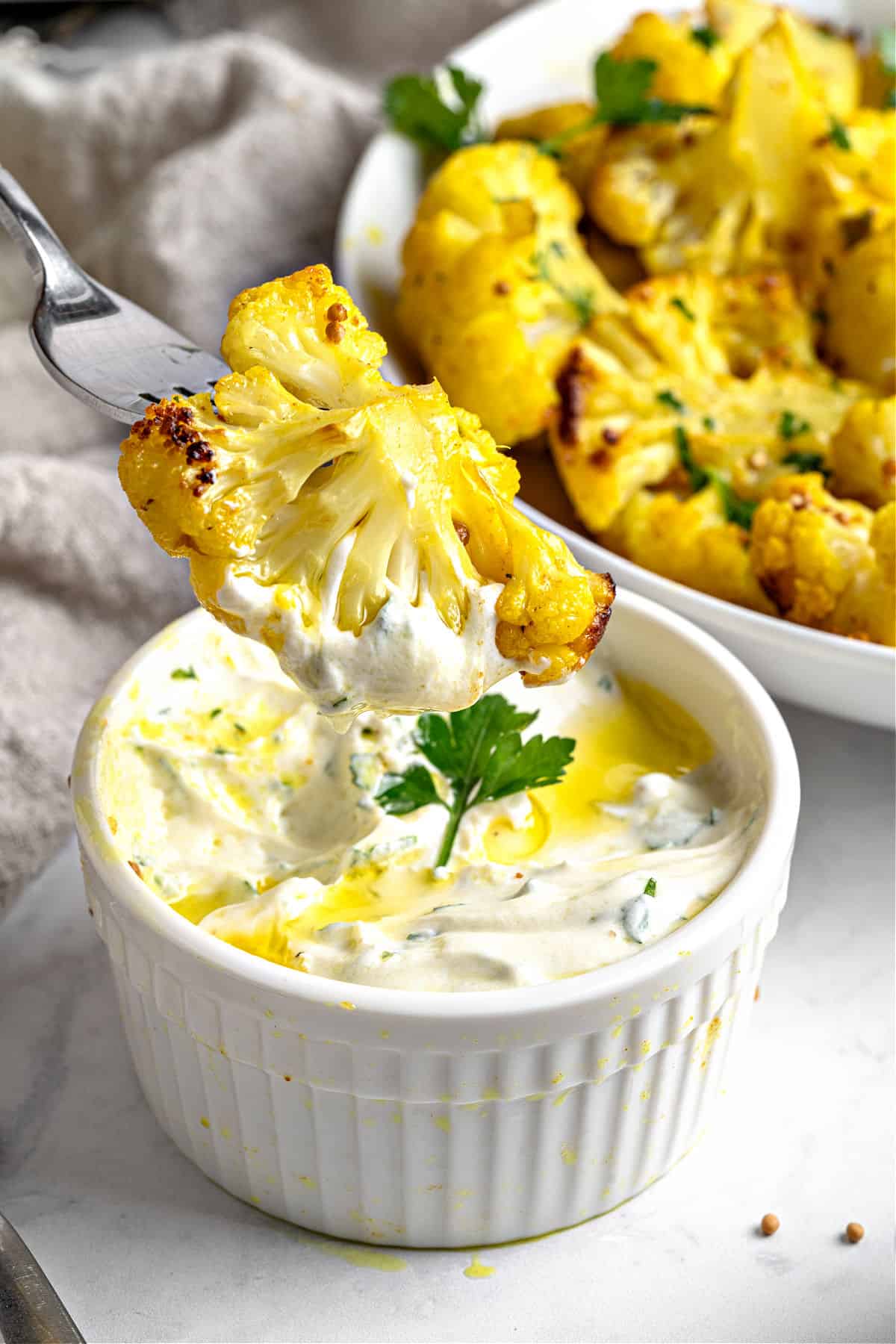 Dipping a bite of cauliflower in a white bowl. Platter in the gray background.