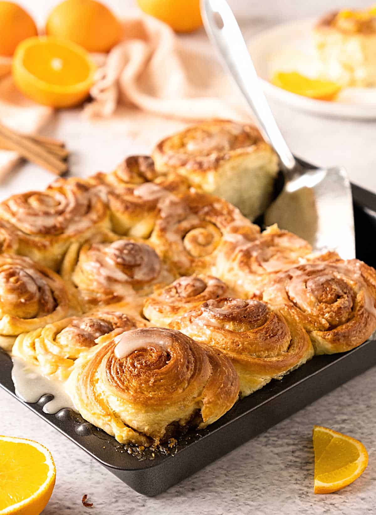 Tray of orange cinnamon rolls on a gray surface. Orange pieces in the background.