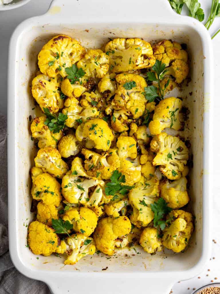 Roasted pieces of spicy cauliflower in a white rectangular baking dish. Top view.