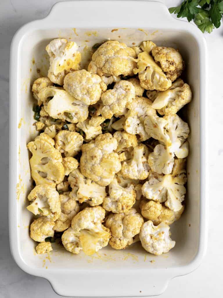 White baking dish with spiced roasted cauliflower pieces before baking.