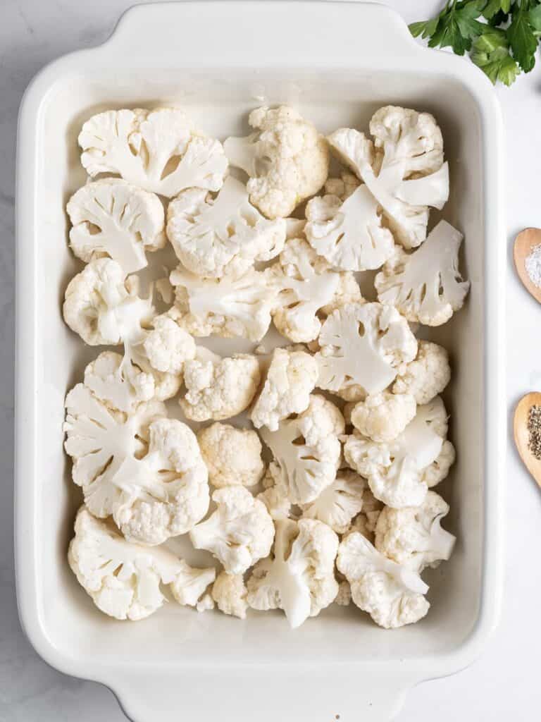 Pieces of cauliflower in a white rectangular baking dish. Top view.