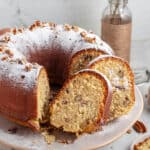 Whole and slices of coconut bundt cake with powdered sugar on a beige plate. Close up image.