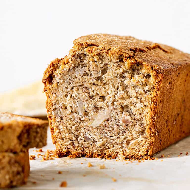 Cut piece of banana bread on white surface and background.