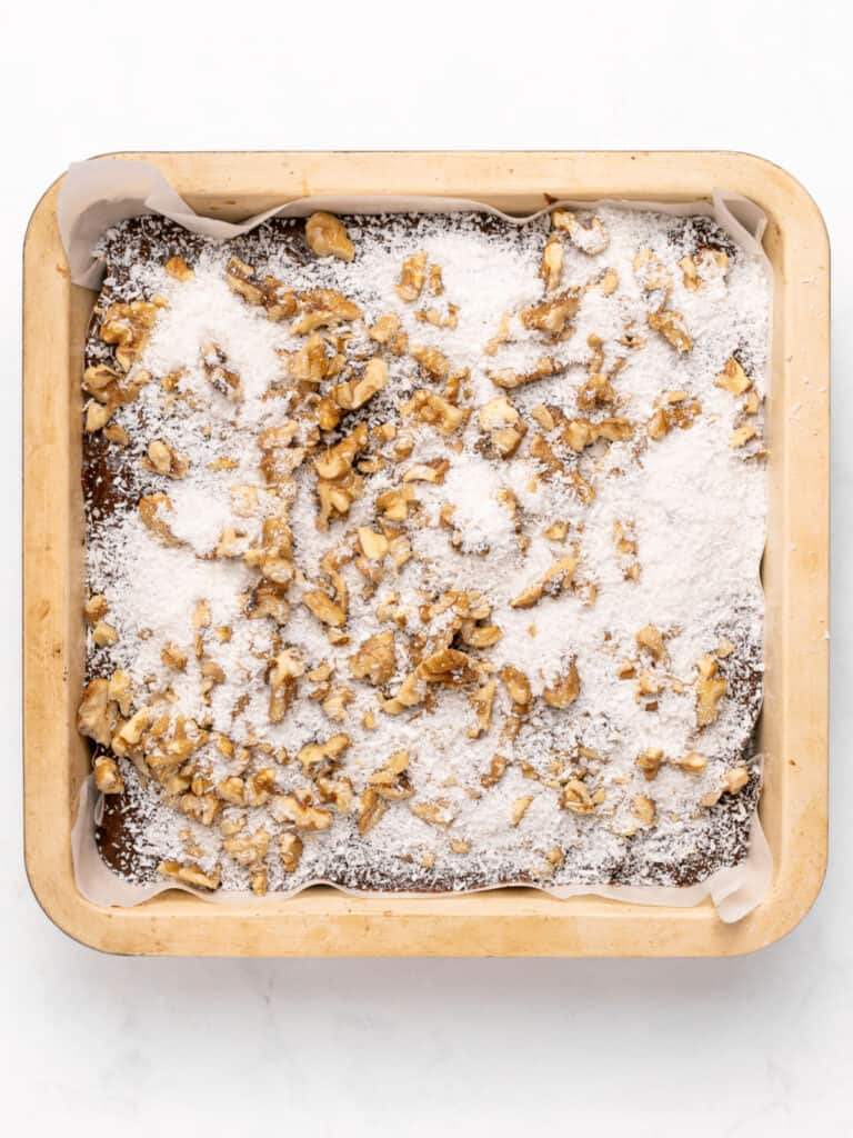 Walnuts and coconut sprinkled over brownie batter in the pan.