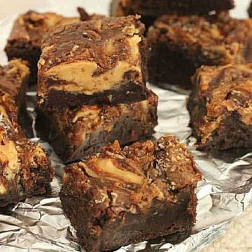 Stacked pieces of swirled brownies on aluminum foil, beige background.