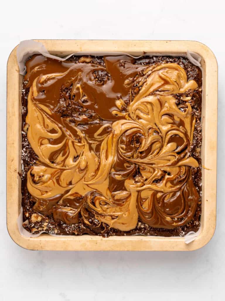 Marbled peanut butter, dulce de leche and brownie batter in a square pan. White background.