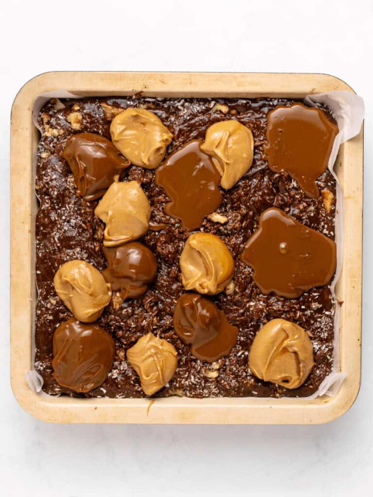 Peanut butter and dulce de leche mounds on top of brownie batter in pan. White background.