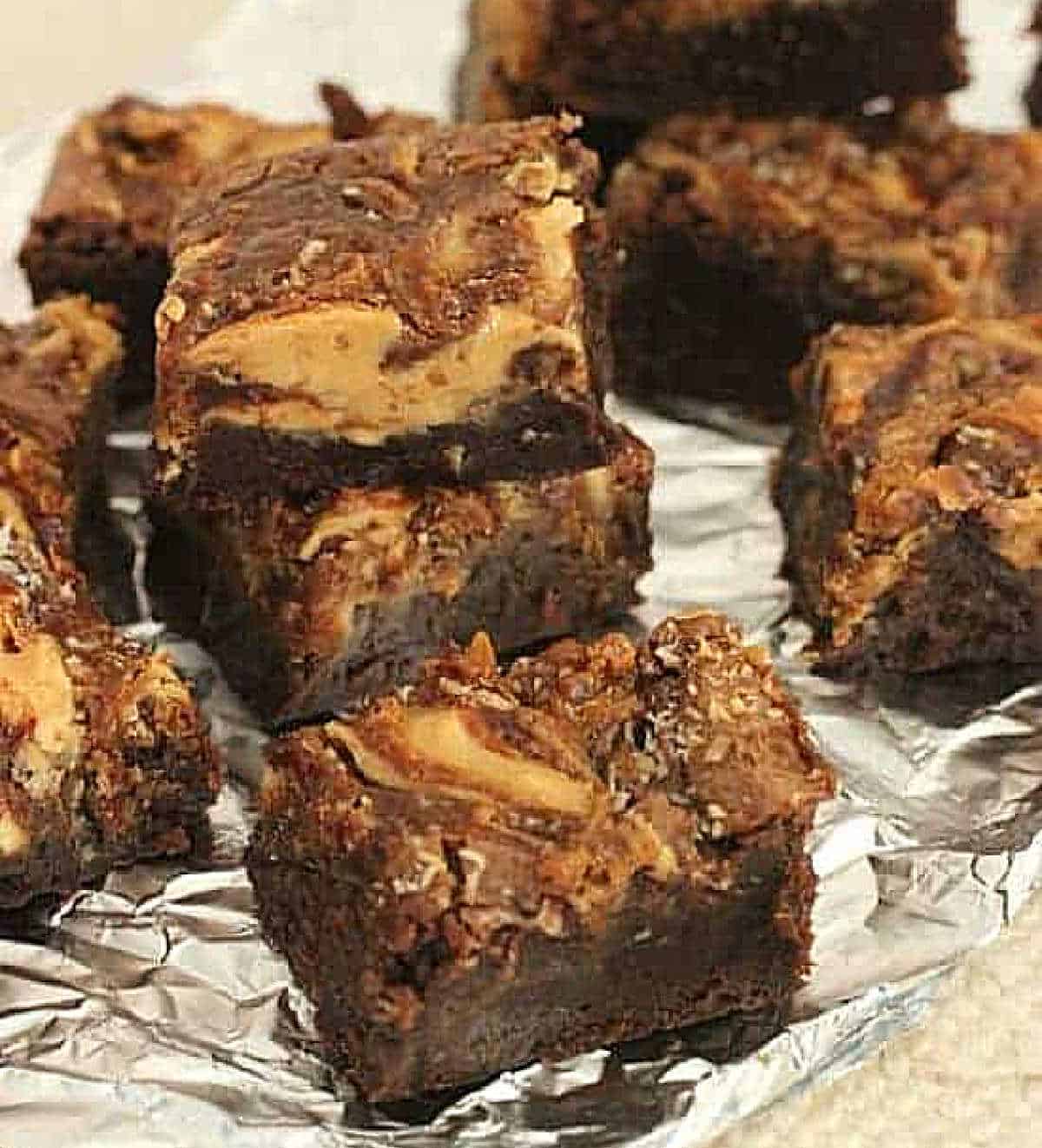 Stacked pieces of swirled brownies on aluminum foil, beige background.