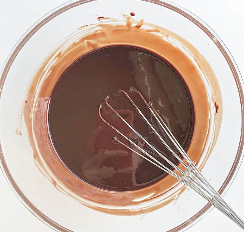 Glass bowl with melted chocolate and butter. A wire whisk. White background.