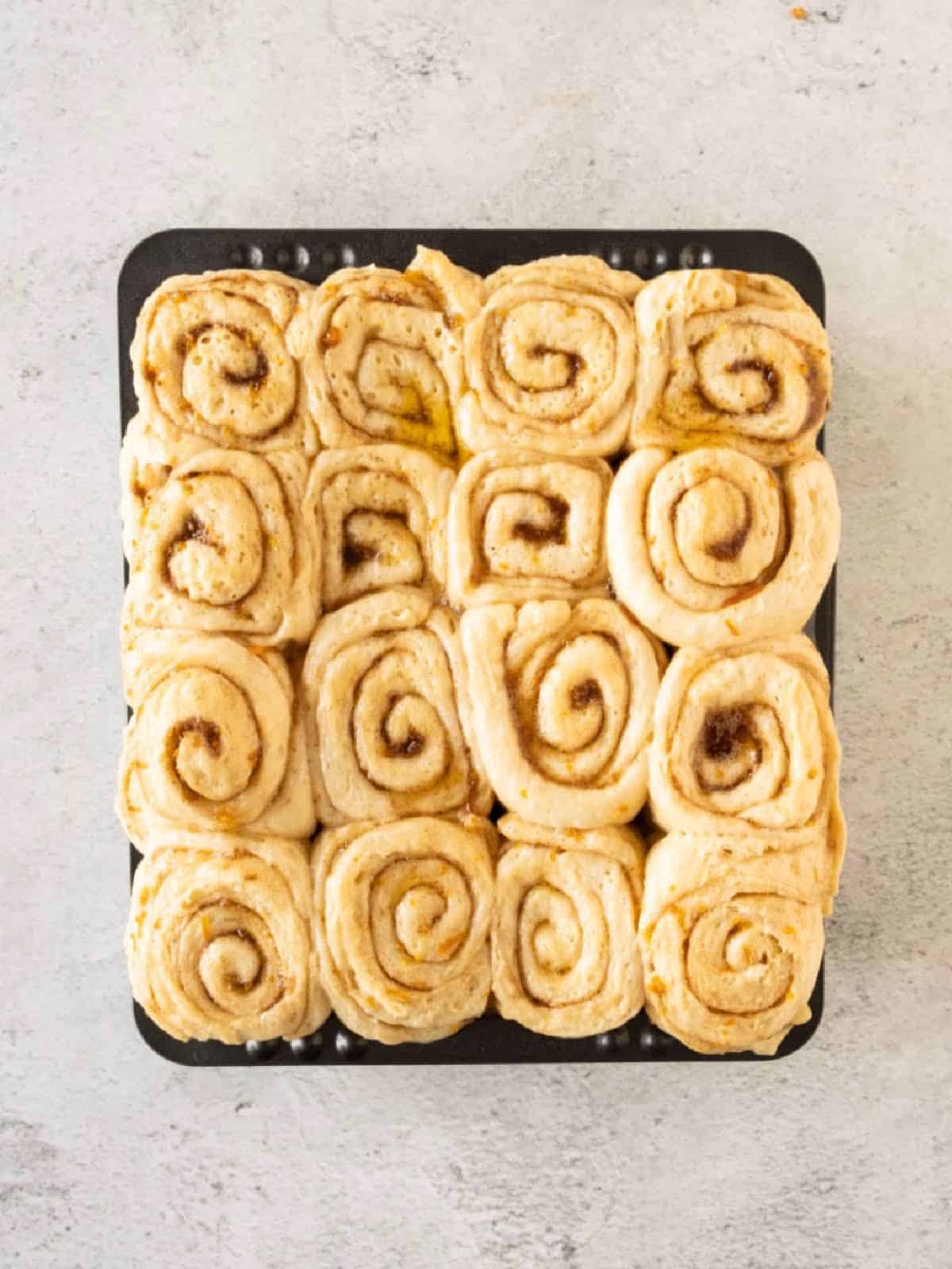 Proofed cinnamon rolls in a black pan on a light gray surface.