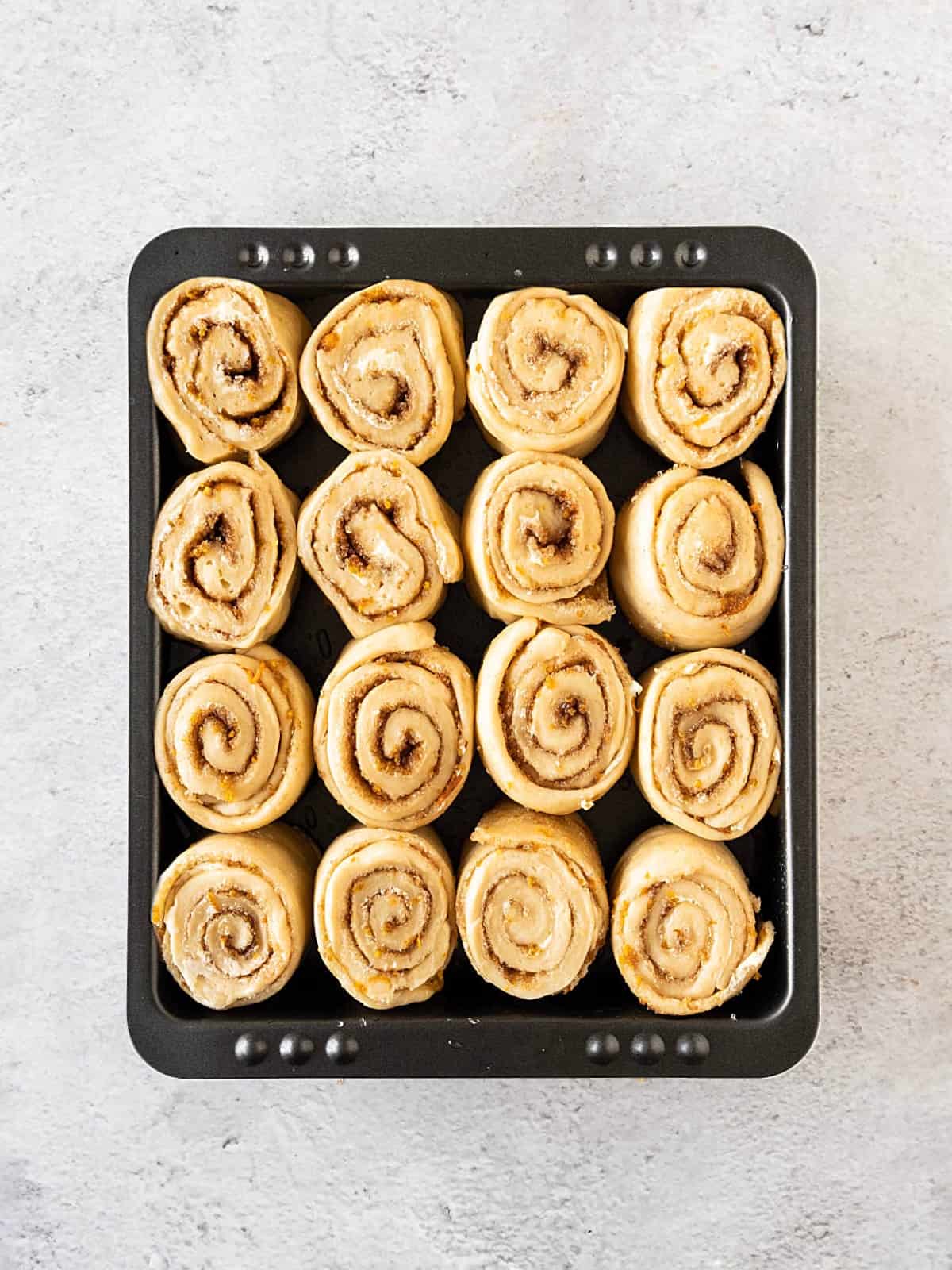 Black pan with cinnamon rolls before the first rise. Light gray surface.