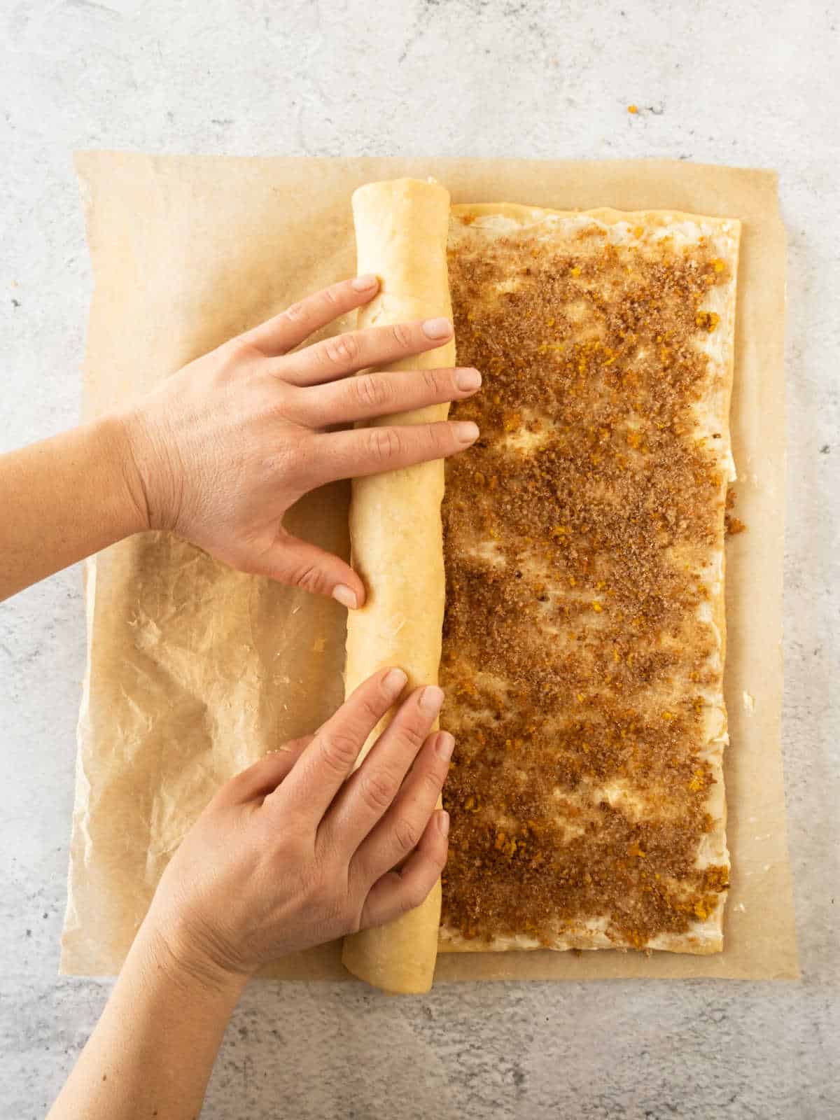 Rolling cinnamon orange rolls dough on parchment paper. Light gray surface.