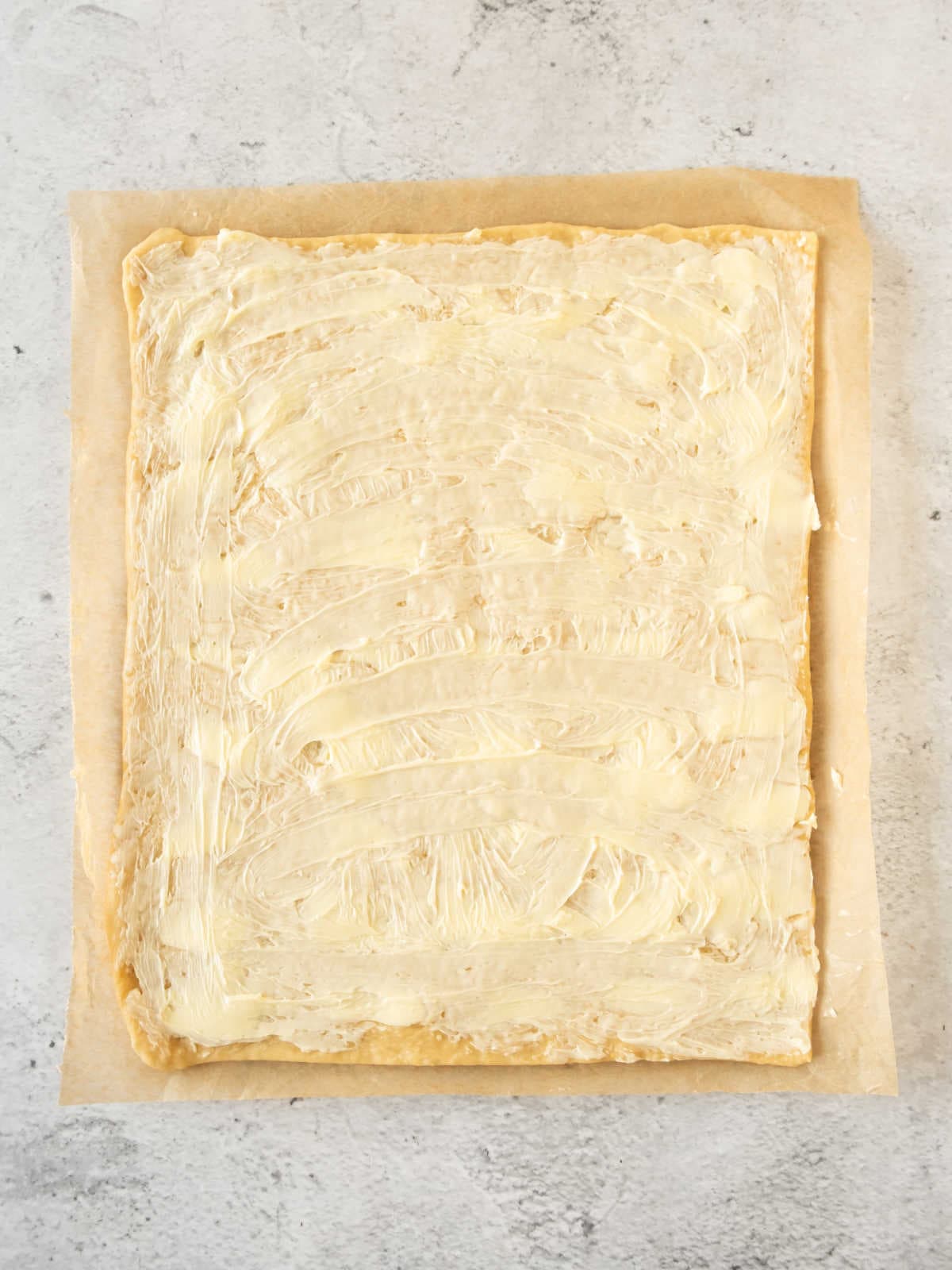 Buttered rectangle of dough on a beige paper. Light gray surface.