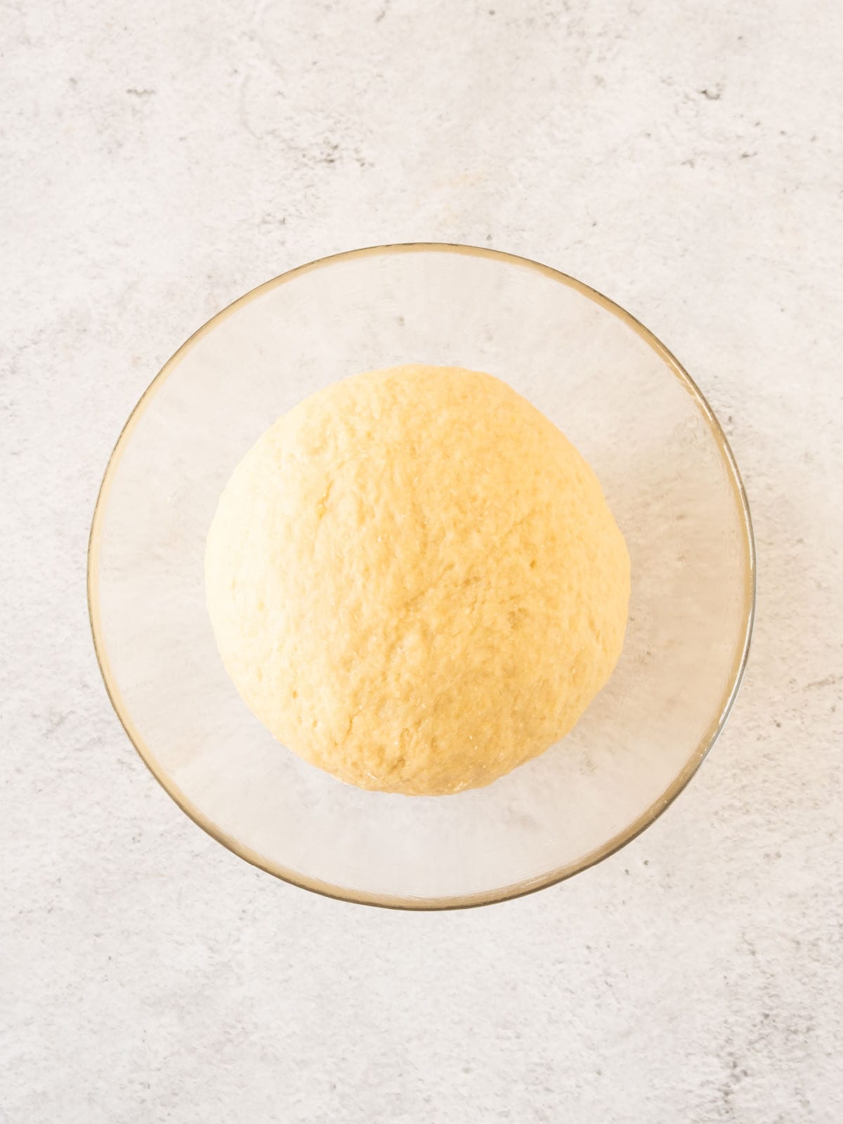 Glass bowl with sweet dough before rising. Light gray surface.