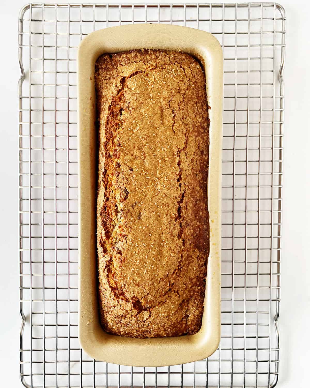 Baked banana bread in a golden loaf pan on a wire rack.