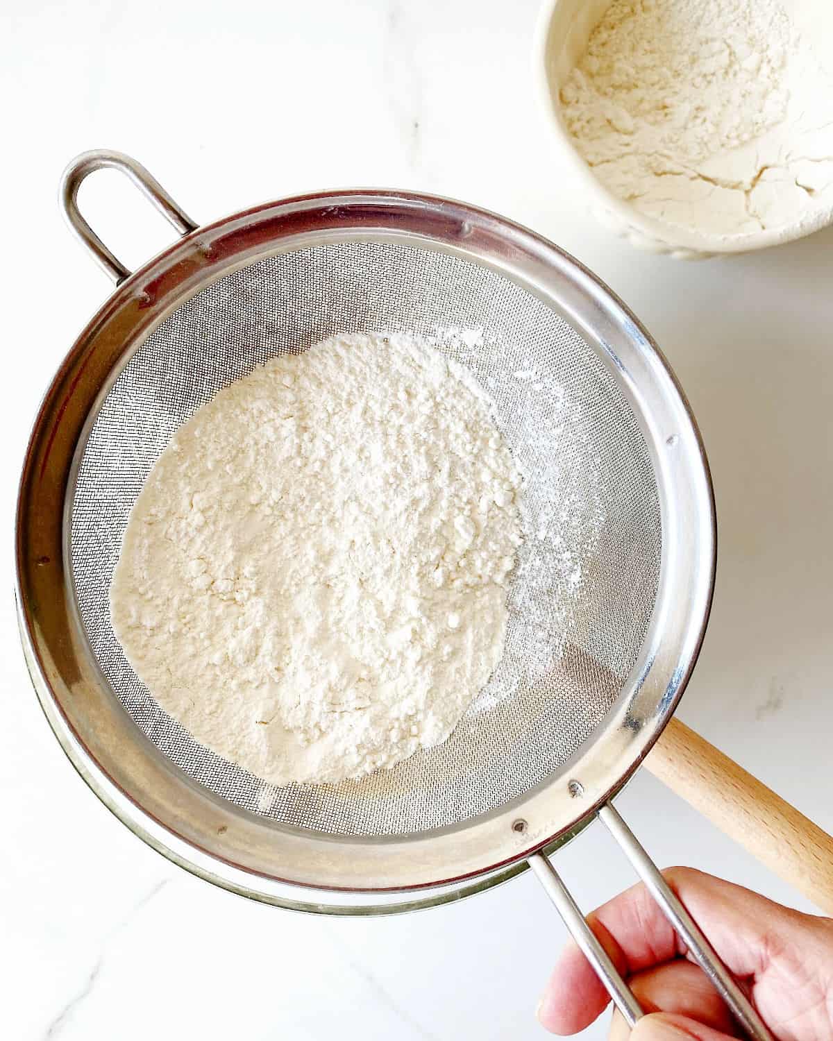 Sifting flour mixture. White surface, white bowl with flour. 
