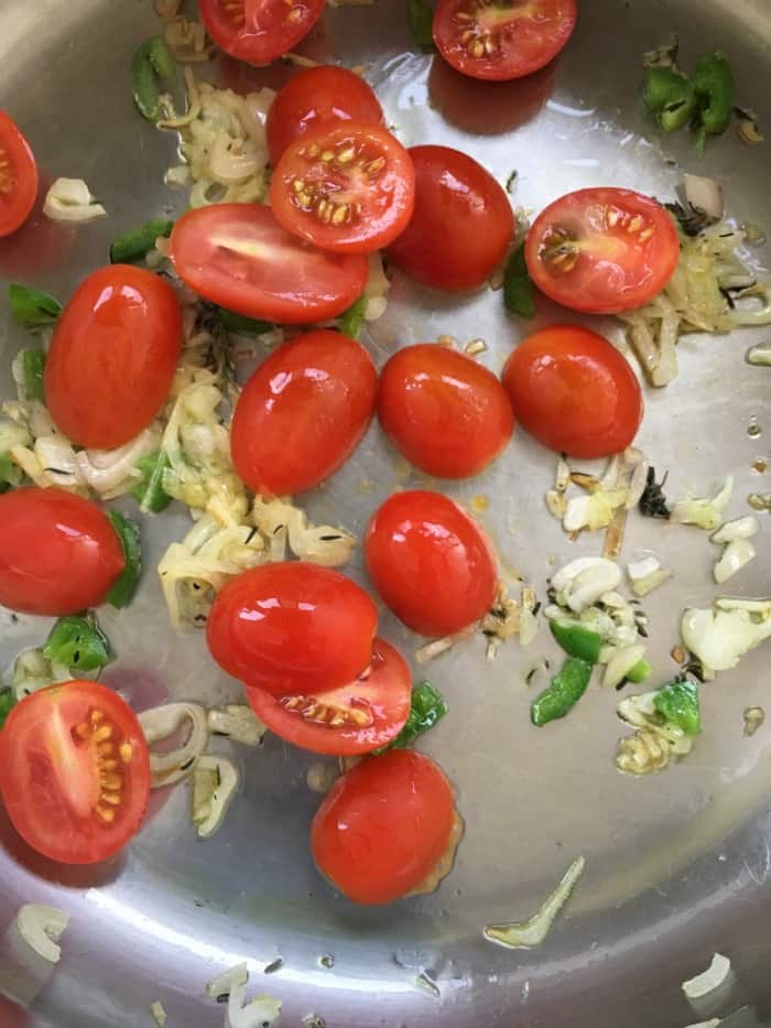 Sauteeing cherry tomatoes and onion on metal skillet.