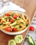 white bowl with pasta and tomatoes on wooden board, white kitchen towel, squeezed limes