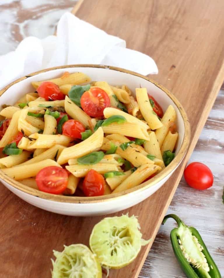 white bowl with pasta and tomatoes on wooden board, white kitchen towel, squeezed limes