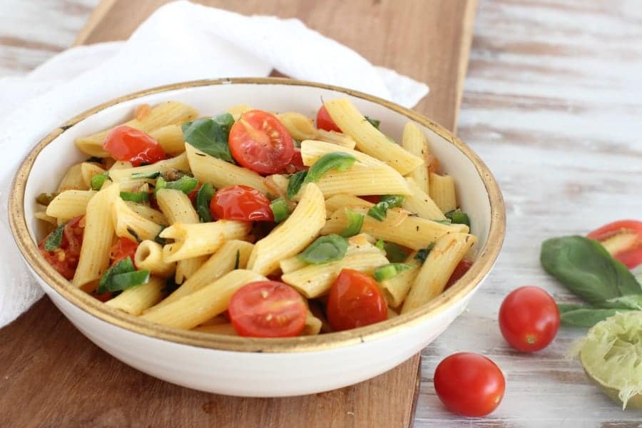 White bowl with pasta and tomatoes, wooden board, white kitchen towel and table