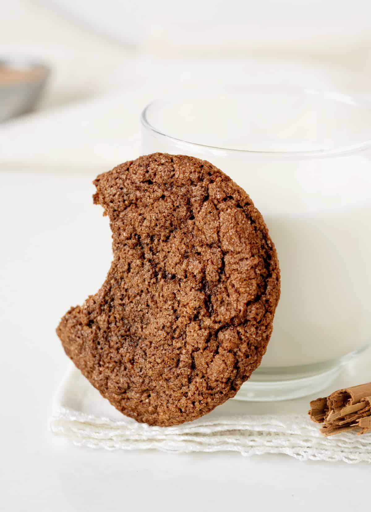 Bitten chocolate cookie leaning on a glass of milk on a white surface. 