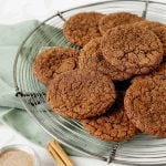 Several chocolate cookies piled on a wire rack with green cloth beneath.