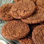 White and red text overlay of chocolate cookies on a wire rack with a green cloth underneath.
