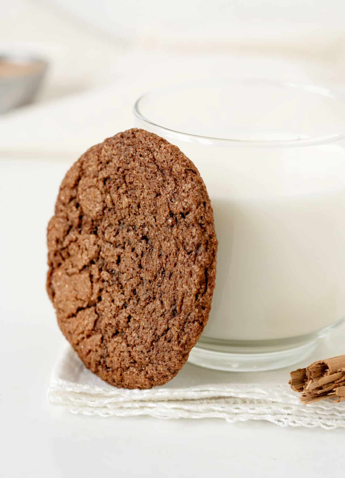 Chocolate cookie leaning on a glass of milk on a white surface.