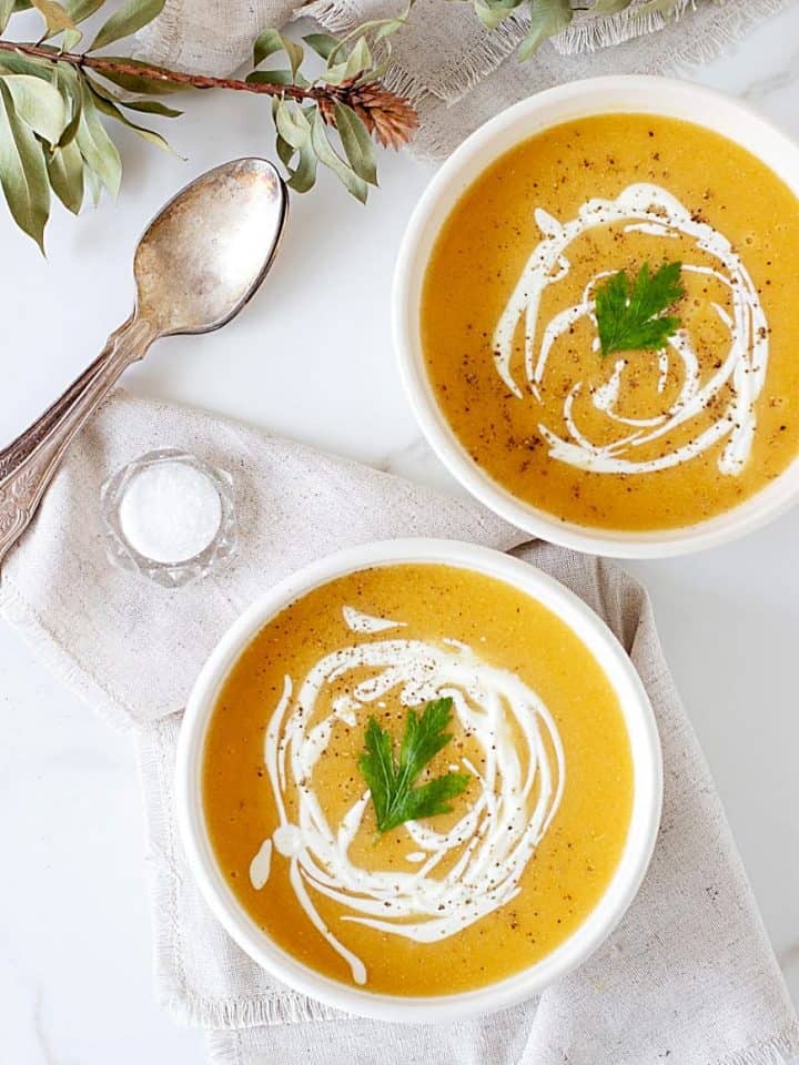 Two white bowls of orange soup, white background, spoons, salt