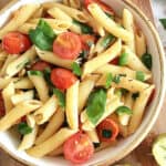 Close up of white bowl with pasta, basil and tomatoes.