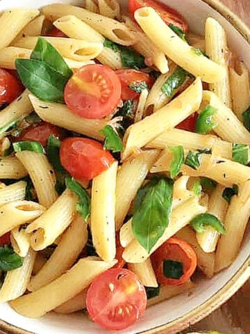 Close up of white bowl with pasta, basil and tomatoes.