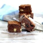 Raisin brownie squares stacked on a whitish table with a blue kitchen towel.