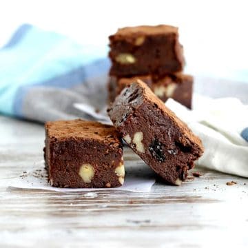 Raisin brownie squares stacked on a whitish table with a blue kitchen towel.