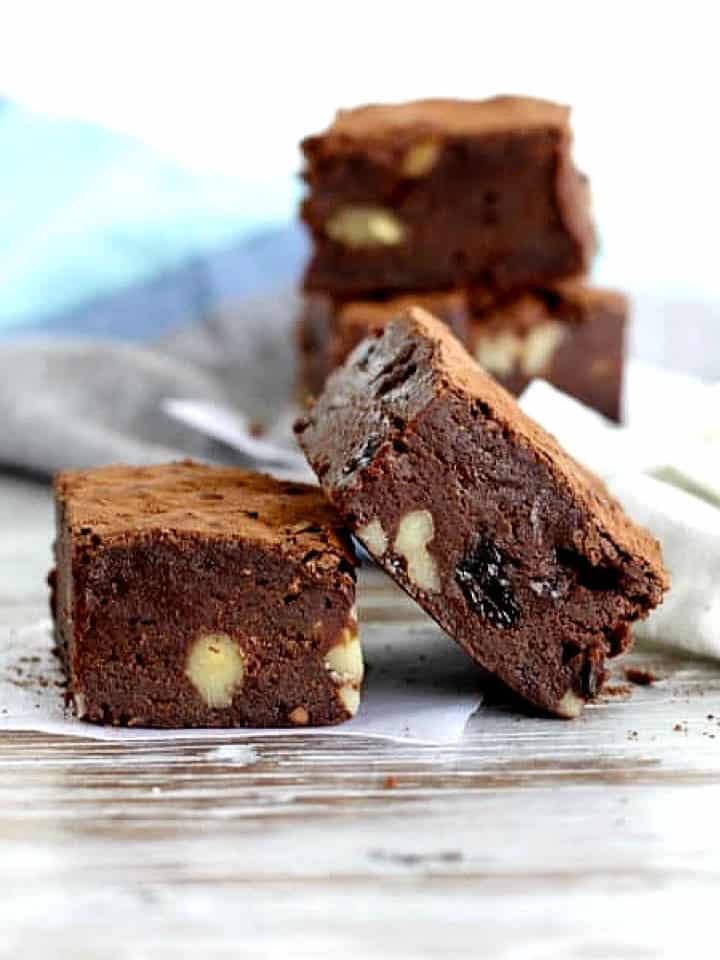 Raisin brownie squares stacked on a whitish table with a blue kitchen towel.
