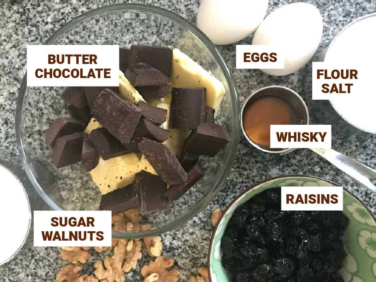 Ingredients for whisky raisin walnut brownies in bowls on a grey counter.