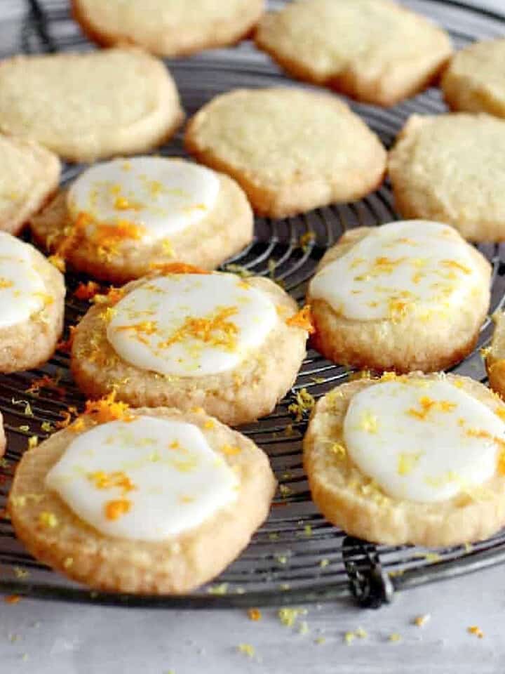 Glazed coconut shortbread rounds on a wire rack with citrus zest on top.