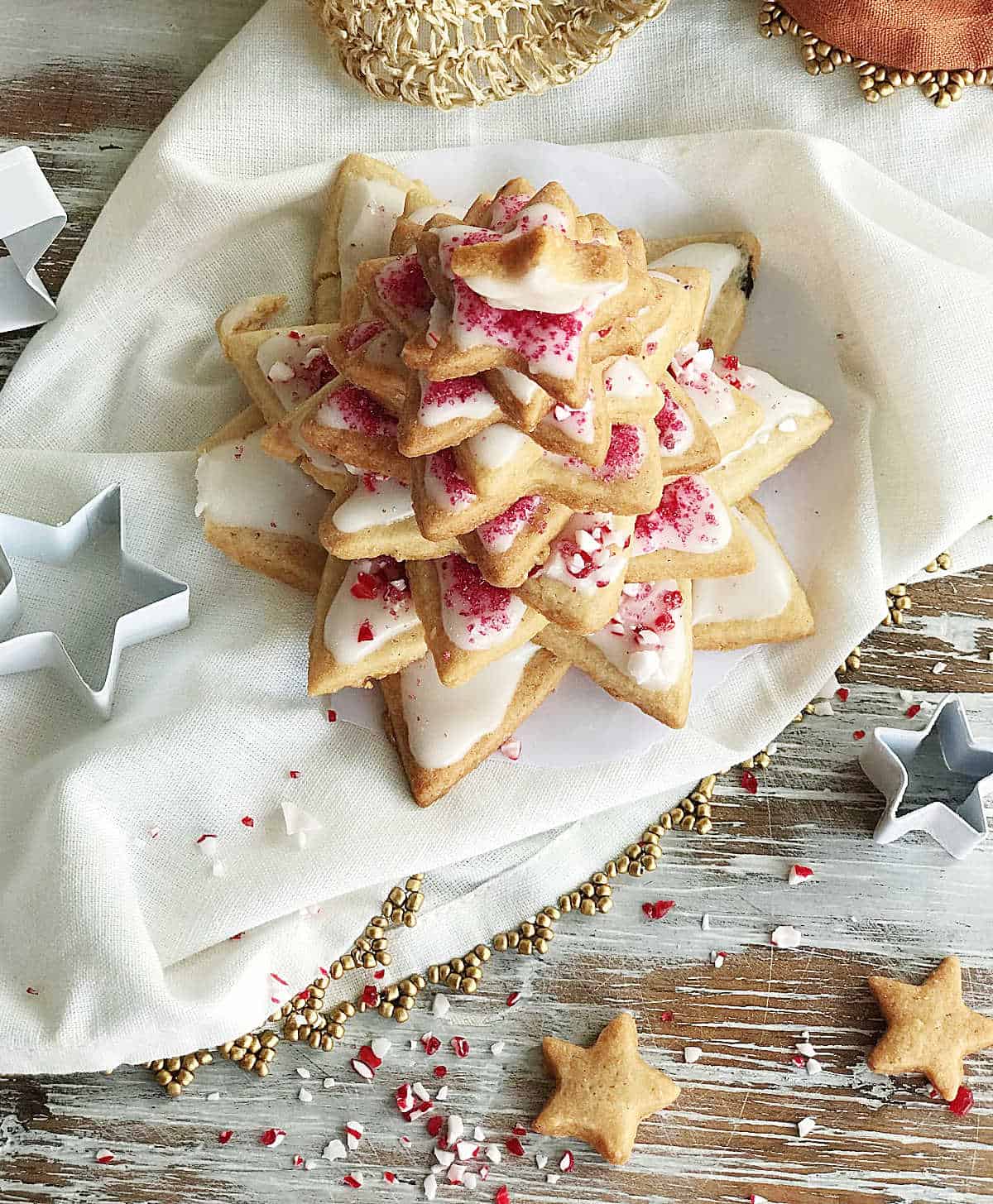 Top view of star shaped cookie Christmas tree, white and gold cloth and props, crushed candy cane scattered