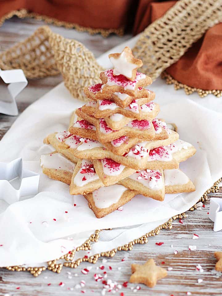 Star shaped Christmas tree made with frosted sugar cookie, candy cane crushed around, white and gold props, surface, and linens