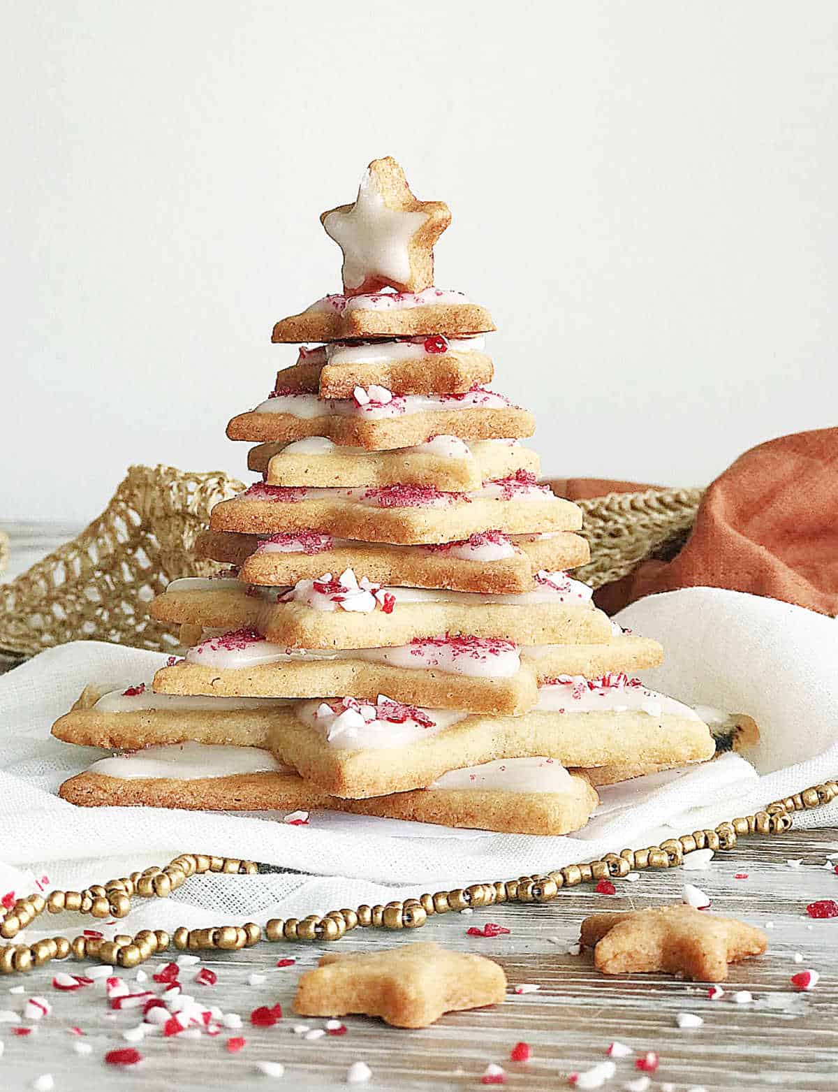 Frontal view of christmas tree made with star shaped cookies, gold white and red props and cloth around.