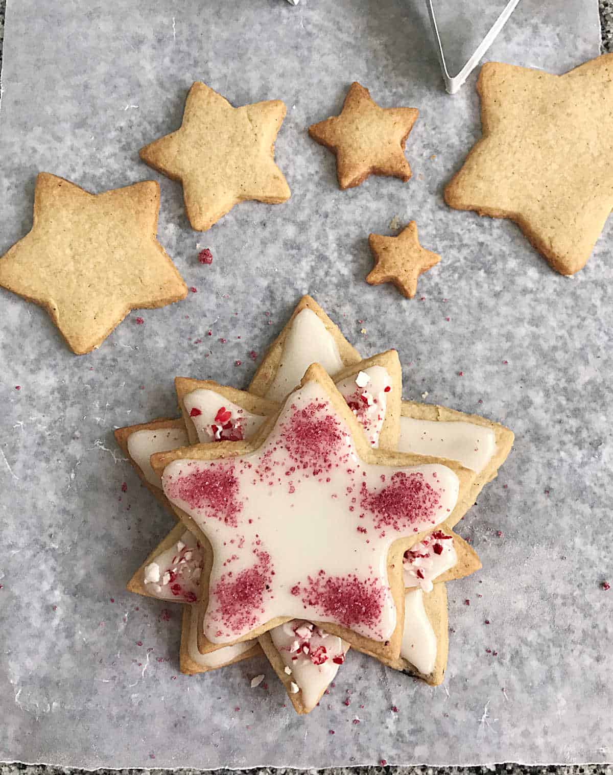 Assembling stacked star shaped cookies with white frosting and crushed candy cane on piece of parchment paper