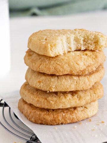 Close up of bitten coconut shortbread butter cookie on top of a stack. White parchment paper and surface.