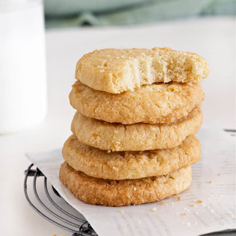 Close up of bitten coconut shortbread butter cookie on top of a stack. White parchment paper and surface.