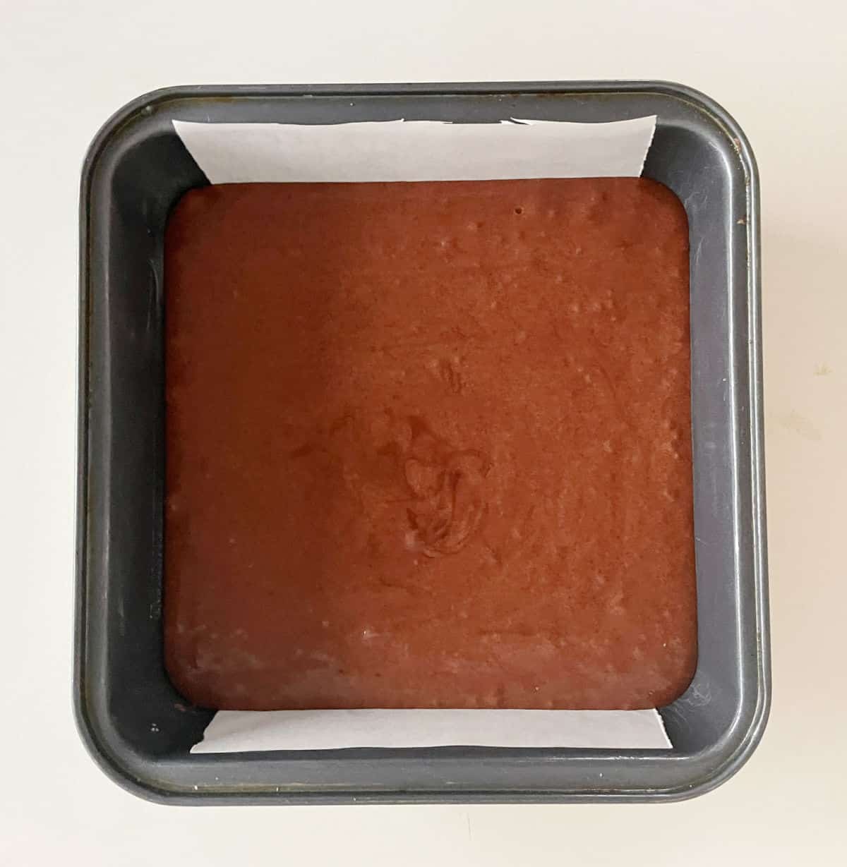 Square pan with brownie batter on a whitish surface. 