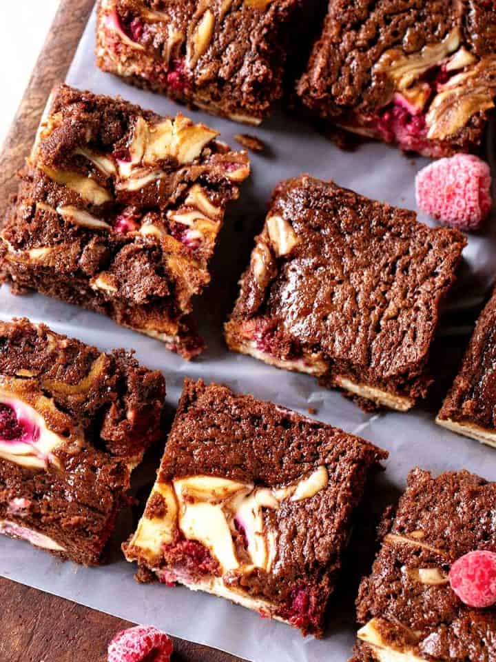 Top view of cheesecake brownie squares with raspberries on a wooden board.
