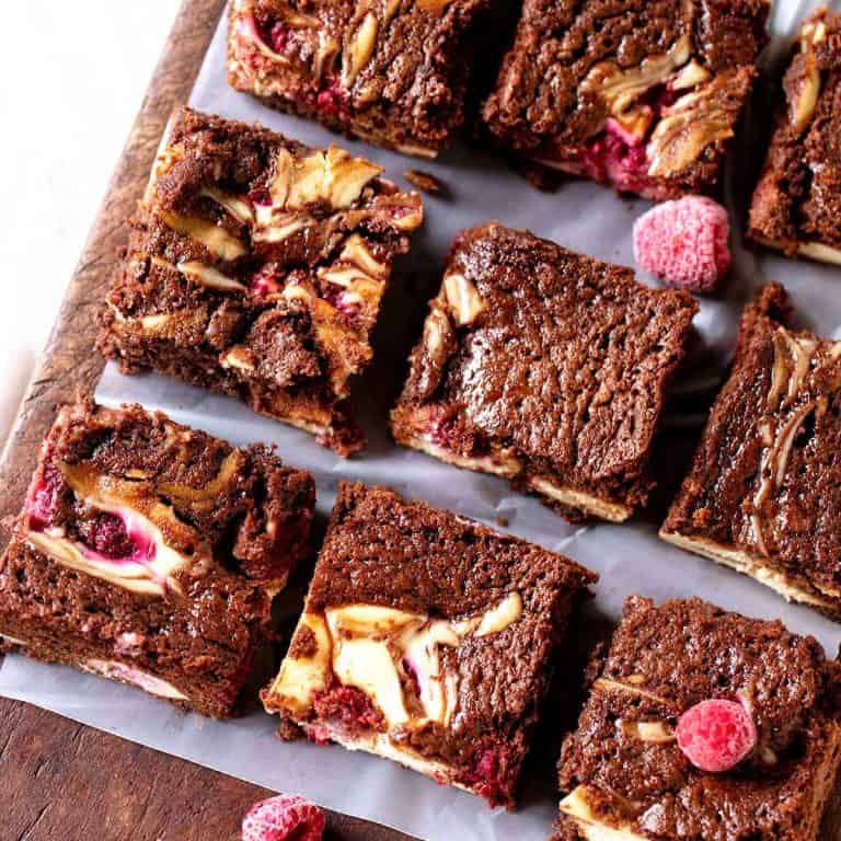Top view of cheesecake brownie squares with raspberries on a wooden board.