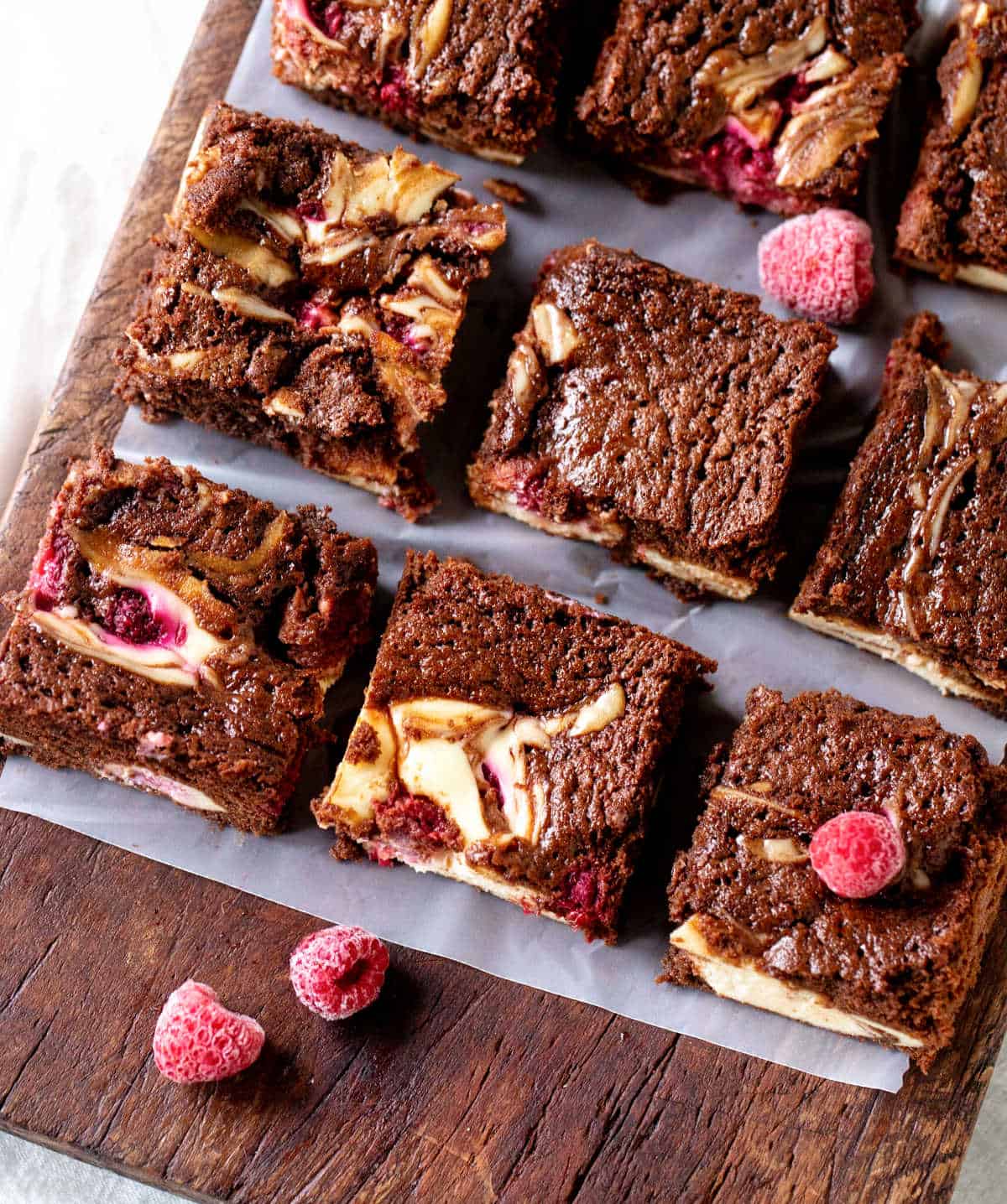 Wooden board with three rows of cheesecake brownies with raspberries.