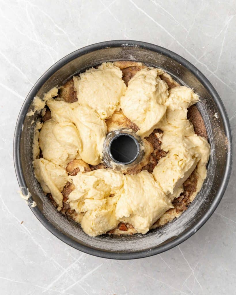 Layering a cinnamon coffee cake in a tube pan on a light grey surface.