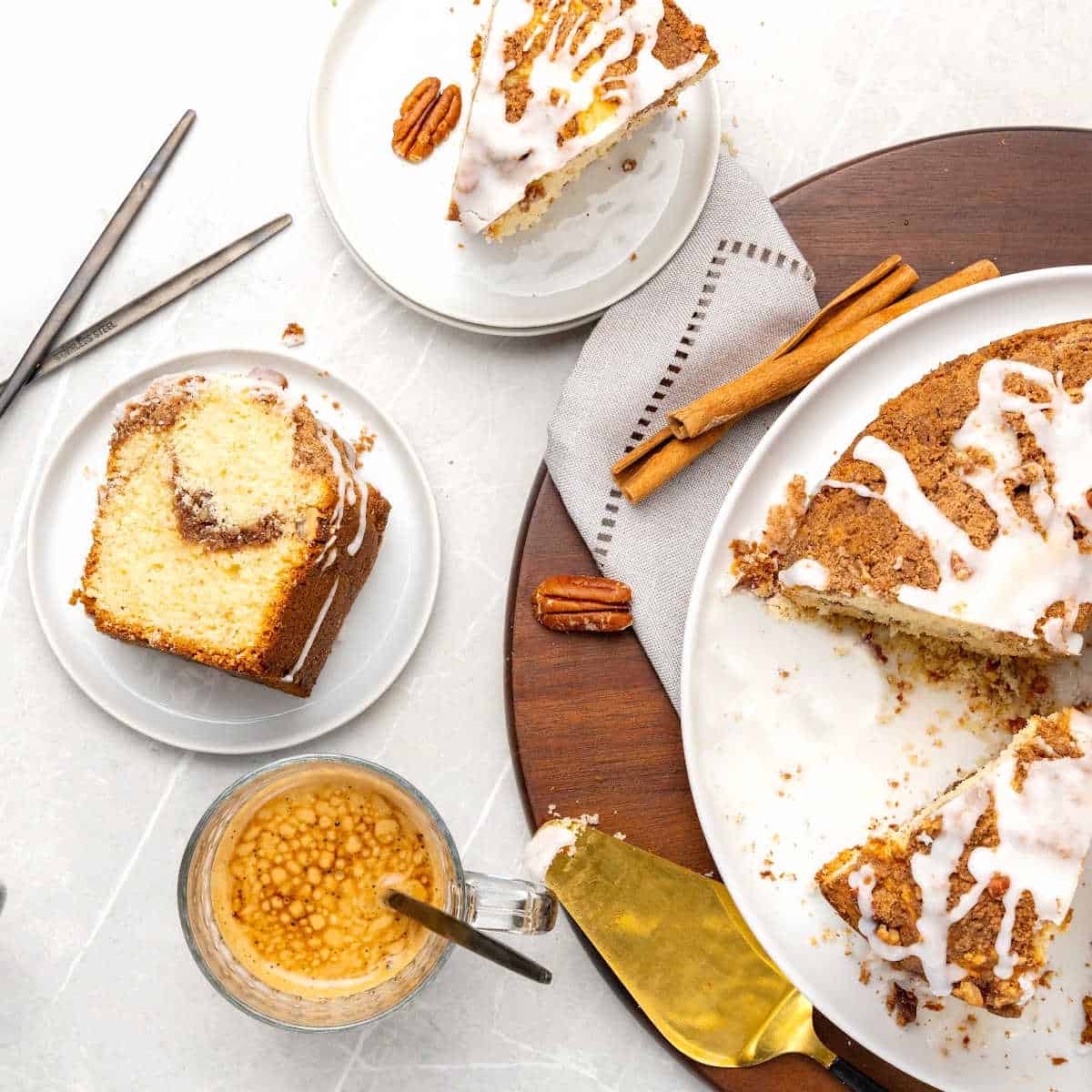 Partial view of glazed coffee cake on a white plate and wooden board. Cake slices on white plates. Light grey surface. 