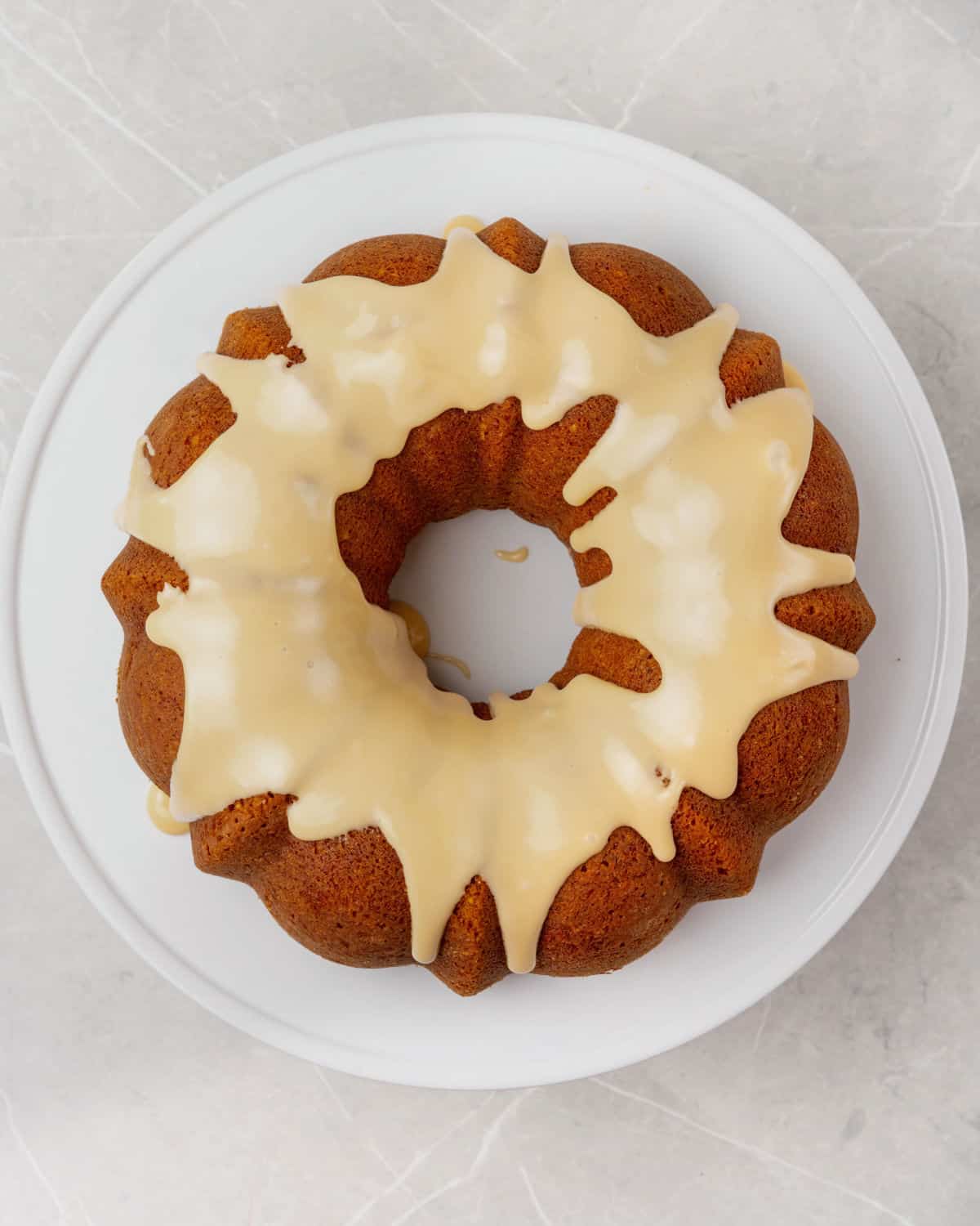 Iced maple walnut bundt cake on a white plate on a grey surface. Top view.